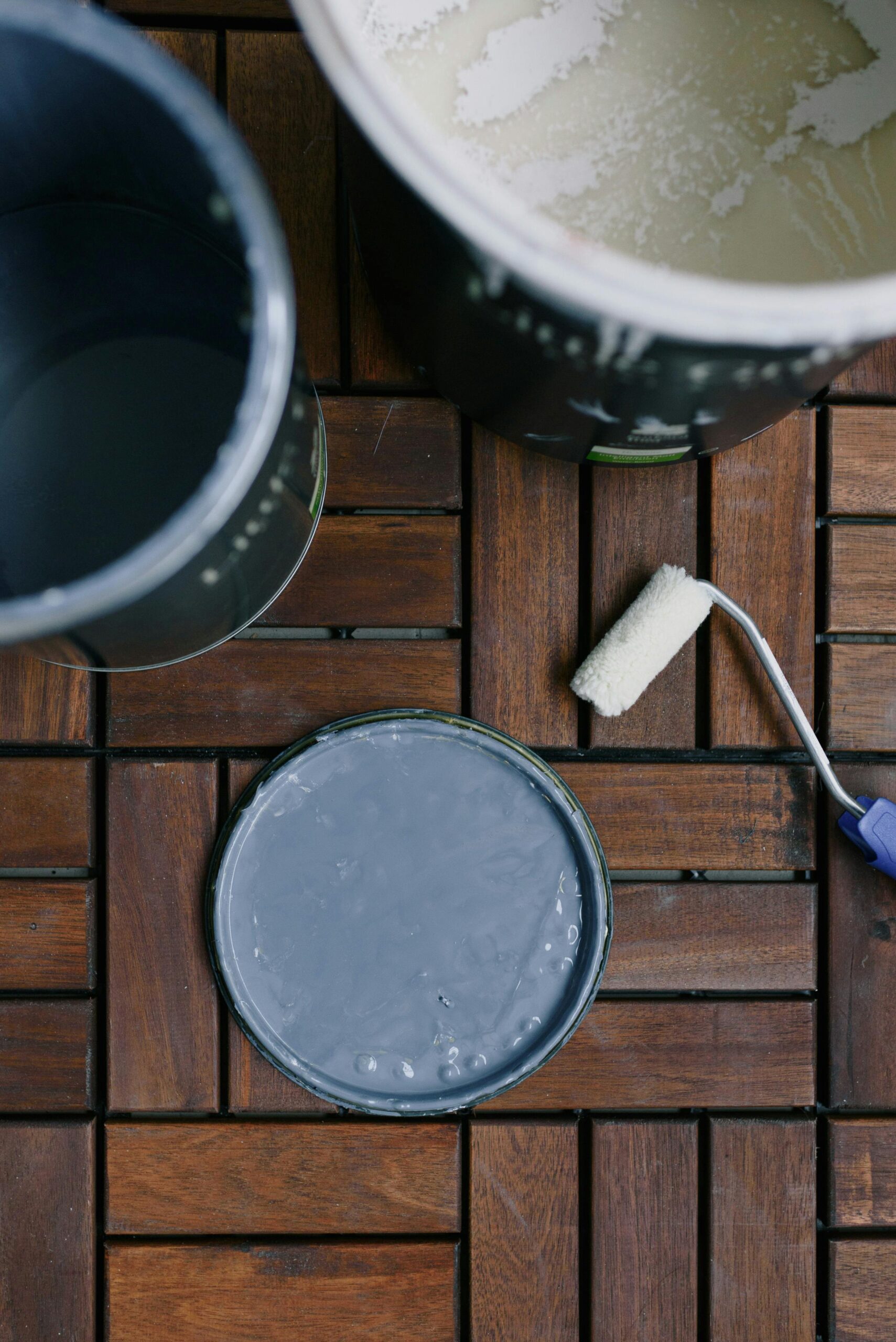 Top view of cans with acrylic paint and clean paint roller on wooden floor at home